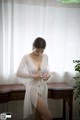 A woman in a white robe standing in front of a window.