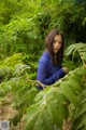 A woman in a blue shirt is standing in the woods.