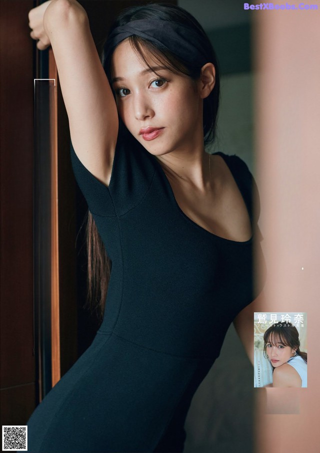 A woman in a black dress leaning against a wall.