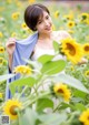 A woman standing in a field of sunflowers holding a blue scarf.