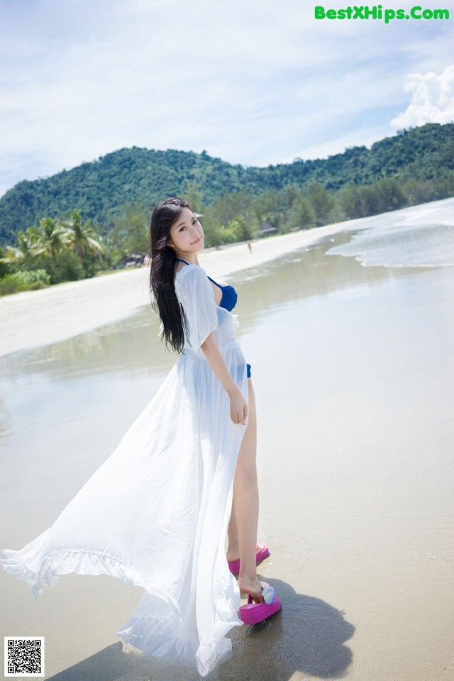 A woman in a white dress standing on a beach.