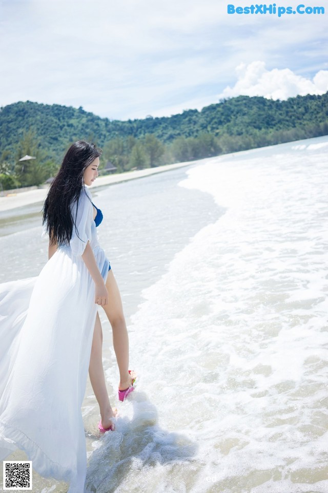 A woman in a white dress standing in the water.
