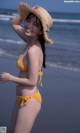 A woman in a yellow bikini and a straw hat on the beach.