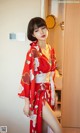 A woman in a red kimono standing in front of a mirror.