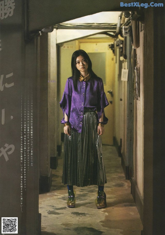 A woman in a purple shirt and black skirt standing in a hallway.