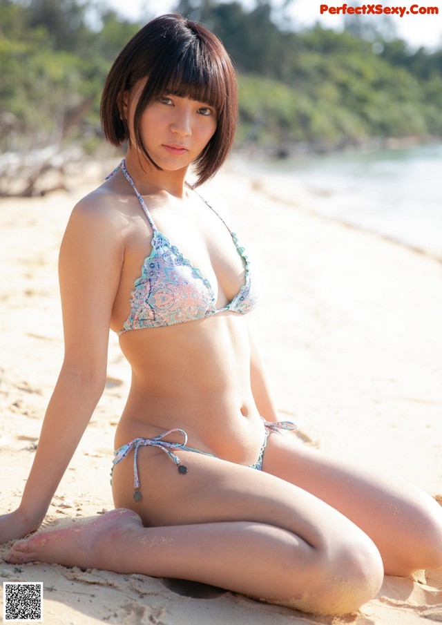 A woman in a bikini sitting on a beach.