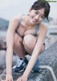 A woman in a gray tank top and red shorts crouching on a rock.