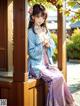 A woman in a blue and purple kimono sitting on a wooden bench.